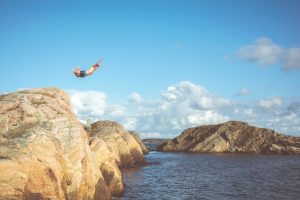 man diving from cliff above ocean